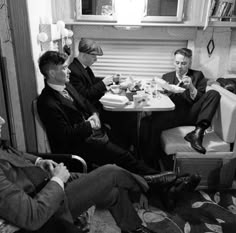 several men in suits and ties are sitting around a table eating food, drinking beer