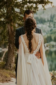 a bride and groom standing next to each other in front of a lake with trees