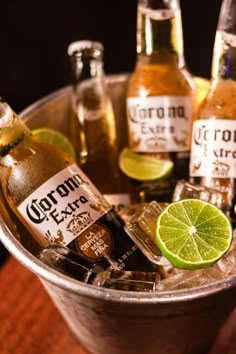 several bottles of corona beer in a bucket with limes and ginger ale on the side