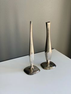 two silver vases sitting on top of a white table