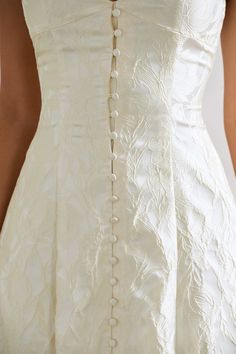 the back of a woman's white wedding dress with buttons and pearls on it