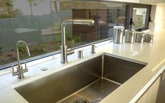 a stainless steel kitchen sink and faucet in front of a window with an outside view