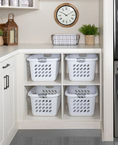 a kitchen with white cabinets and baskets in front of a clock on the wall above it