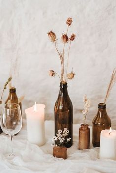 several vases with flowers and candles are arranged on a bed sheet in front of a white wall