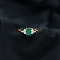 an emerald and diamond ring sitting on top of a black cloth