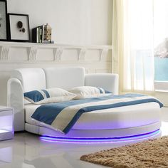 a white bed with blue lights on it in a room next to a window and rug