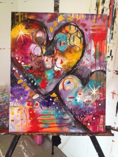 an abstract painting with hearts and stars in the center on a easel next to paintbrushes