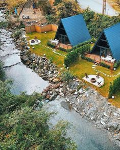 an aerial view of two cabins in the woods next to a river and forest area