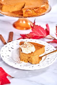 a slice of pumpkin pie on a white plate next to fall leaves and cinnamon sticks