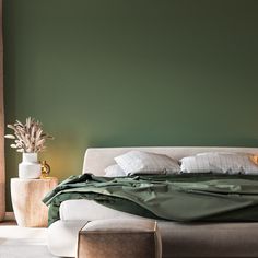 a bed with green sheets and pillows in a room next to two vases on the floor