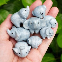 small elephant figurines sitting in the palm of someone's hand with green leaves behind them