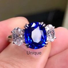 an oval blue sapphire surrounded by three smaller round diamonds on top of a hand with the words unique written below it