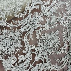 an embroidered lace fabric with white flowers and leaves on the bottom, is shown in close up