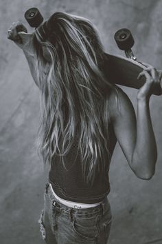 a woman with long hair holding a skateboard over her head and looking at the camera