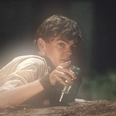 a young man laying on top of a wooden log holding a glass in his hand