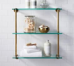 two glass shelves with towels, soaps and other items on them against a white brick wall