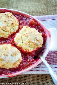 three biscuits are placed on top of some strawberry cobbler crumblers in a red dish