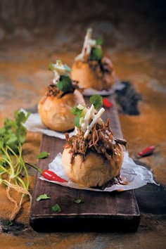 three small sandwiches with meat and vegetables on them sitting on a cutting board next to other food items