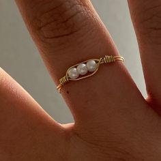 a woman's hand wearing a gold ring with two pearls on the middle finger