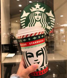 a person holding up a starbucks cup in front of a starbucks sign with a woman's face on it