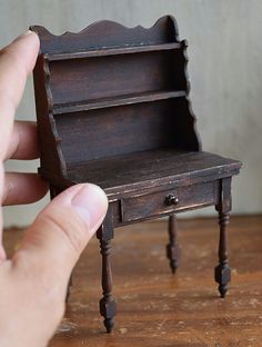 a hand holding a miniature wooden shelf on top of a table next to a small drawer