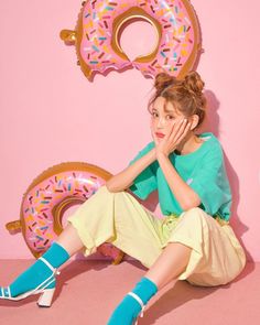 a woman sitting on the ground next to a pink wall with donuts in it