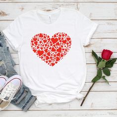 a white t - shirt with red hearts printed on the front and back, sitting next to a rose