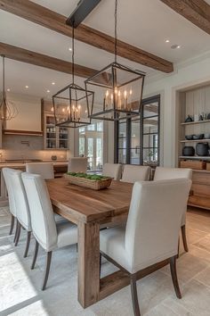 a dining room table with chairs and lights hanging from it's beams in front of an open kitchen