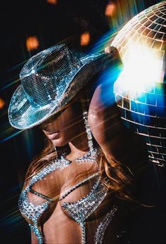 a woman with a disco ball and hat in front of a mirror wall at night