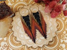 a pair of beaded earrings sitting on top of a doily next to a piece of cake