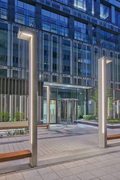 an empty plaza with benches and lights in front of a building