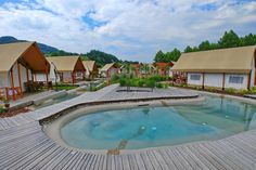 there is a hot tub in the middle of this wooden decked area with several cabins behind it