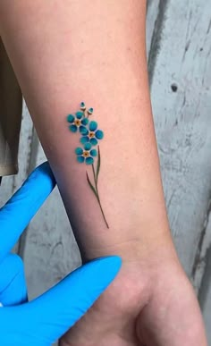 a blue flower tattoo on the left inner arm is shown in front of a person's hand