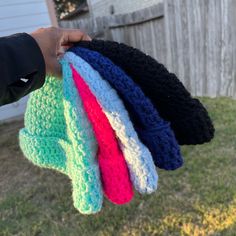 a person holding five crocheted hats in their left hand and the other one is wearing a black shirt