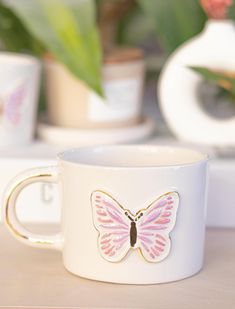 a white coffee cup with a pink butterfly on the inside and gold trim around it