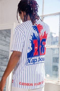 a man with dreadlocks standing in front of a window wearing a baseball jersey