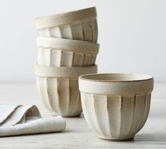 four white bowls sitting next to each other on top of a wooden table with napkins