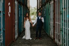 a bride and groom holding hands in an open area with shipping containers on either side