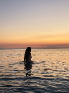 a woman is sitting in the water at sunset with her back turned to the camera