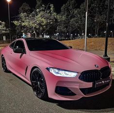 a pink car is parked on the side of the road at night with street lights in the background