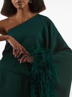 The Taller Marmo Eternity Dress is a sophisticated piece featuring an asymmetrical neckline and a one-shoulder silhouette. It has a single long sleeve with a feather trim and a column silhouette. The dress has a straight hem and a long length. It is made in Italy.