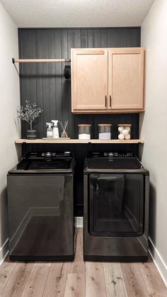 two black appliances in a small kitchen with wood flooring and cabinets above the washer and dryer