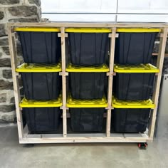 several black plastic bins are stacked up on a wooden shelf in front of a brick wall