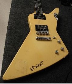 an old yellow guitar with writing on it sitting on the floor next to a black carpet