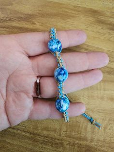 a hand holding a blue beaded bracelet on top of a wooden table next to a key