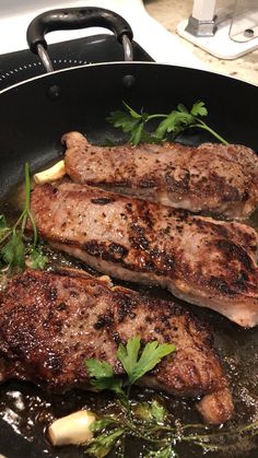 two steaks cooking in a skillet on top of a stove with herbs and water