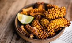 corn on the cob in a bowl with lime wedges next to it and an open book