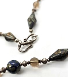 Apache pyrite, lapis lazuli and smoky quartz beaded sterling silver artisan necklace. The beads on this unique necklace are one of a kind. Each gemstone bead is unique in the pyrite inclusions that are found through out the stones. The Apache pyrite elongated bicone beads are full of amazing color and heavy. The lapis lazuli is mottled with a large amount of shining gold highlights through the blue lapis. There are sterling silver and smoky quartz beaded spacers between. Stamped 925 on the hook Silver Sterling Silver Gemstone Beaded Necklaces, Silver Sterling Beaded Necklaces With Gemstone Beads, Silver Sterling Silver Necklace With Gemstone Beads, Unique Sterling Silver Jewelry With Polished Beads, Handmade Earthy Silver Jewelry, Earthy Handmade Silver Jewelry, Adjustable Silver Earthy Necklaces, Silver Labradorite Beaded Necklace For Gifts, Artisan Sterling Silver Necklace With Polished Beads