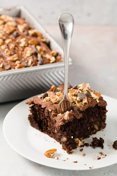 a piece of chocolate cake on a plate with a spoon in it and a pan behind it