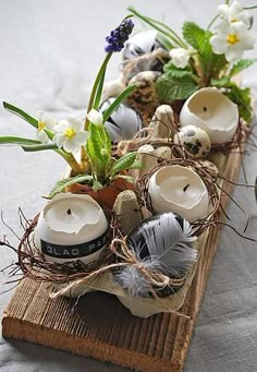 some white candles are sitting on a wooden tray with flowers and feathers in them,